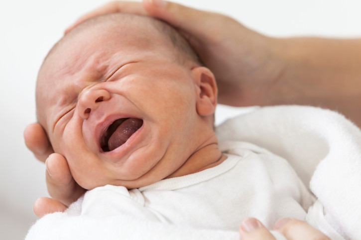 bebe llorando y mano de adulto sujetando la cabeza